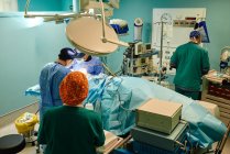 From above back view of unrecognizable medical assistant leaving operating room while group of doctors performing surgery in modern clinic — Stock Photo