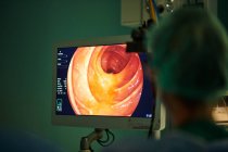 Повернення до нерозпізнаної жінки-лікаря у формі, який дивиться на монітор під час виконання ендоскопічної хірургії в сучасній операційній кімнаті. — стокове фото