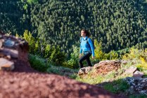 Traveling female with backpack trekking in rocky terrain in mountains on sunny day and looking away — Stock Photo