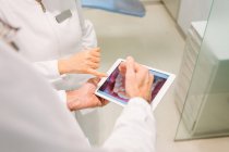 Von oben schneiden anonyme Zahnärzte in medizinischen Gewändern, die den Zustand der Zähne auf einem Röntgenbild auf einem Tablet untersuchen, während sie in einer modernen Zahnklinik zusammenarbeiten — Stockfoto