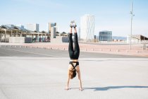 Back view full length fit determined sportswoman in tight activewear doing handstand exercise on asphalt road on sunny suburb — Foto stock
