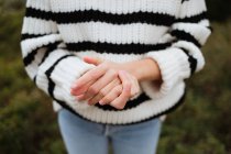 Crop anonymous female tourist in knitted sweater with ornament showing friendship gesture on mountain in daylight - foto de stock