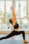 Young flexible female in sportswear standing in Trikonasana pose while practicing yoga with raised arm and looking up in house — Foto stock