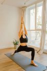 Junge flexible Frau in Sportkleidung steht in Trikonasana-Pose, während sie Yoga mit erhobenem Arm praktiziert und im Haus nach oben schaut — Stockfoto
