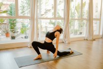 Анонімна жінка в спортивному одязі спирається на килимок, практикуючи йогу біля вікна вдома — стокове фото