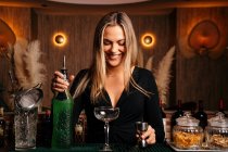 Verführerische junge Barkeeperin mit langen blonden Haaren bereitet am Tresen einen Cocktail aus Alkohol zu — Stockfoto