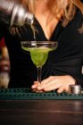 Camarera femenina sin rostro en traje elegante verter cóctel de alcohol de coctelera en elegante vaso de margarita en el restaurante - foto de stock
