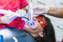 Cosecha dentista anónimo en guantes usando herramienta de luz de curado ultravioleta dental durante el procedimiento con el paciente en la clínica - foto de stock
