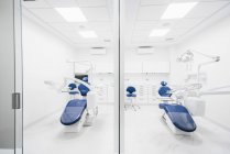 Інтер'єр сучасної охайної стоматологічної клініки з синім стільцем та білими меблями, обладнаними сучасною стоматологічною машиною та інструментами — стокове фото
