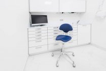 Стильный дизайн интерьера современной светлой клиники с белой мебелью и синим креслом — стоковое фото