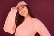 Portrait of happy young asian woman in the studio wearing pink clothes over garnet background — Stock Photo