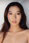 Porträt einer nackten jungen Chinesin, die vor weißem Hintergrund in die Kamera blickt — Stockfoto