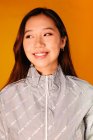 Retrato de mulher jovem asiática com expressão séria. Ela usa uma jaqueta cinza e está olhando para o fundo amarelo — Fotografia de Stock