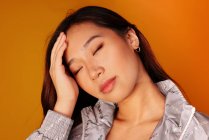 Волнуется китайская молодая женщина с закрытыми глазами на желтом фоне — стоковое фото