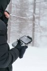 Cropped unrecognizable male wearing warm black jacket with hood standing on snowy terrain with drone remote control — Stock Photo
