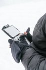 Masculino irreconocible con chaqueta negra cálida con capucha de pie en terreno nevado con control remoto de drones - foto de stock
