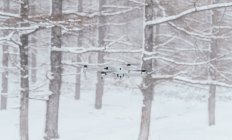 Сучасний білий безпілотник літає над засніженою галявиною в замерзлому зимовому лісі вдень — стокове фото