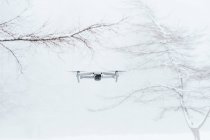 Zeitgenössische weiße Drohnen fliegen bei Tageslicht über verschneite Lichtungen in gefrorenen Winterwäldern — Stockfoto