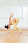 Full body side view of focused female bending forward with leg on tiptoe in Standing Forward Bend with Shoulder Opener asana — Stock Photo