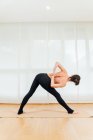 Visão traseira corpo inteiro de mulher sem camisa irreconhecível em pernas de alongamento de pernas pretas e melhorar a flexibilidade durante a prática de ioga — Fotografia de Stock