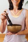 Crop smiling female playing on Tibetan singing bowl while for relax and meditation in studio — Stock Photo