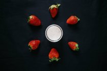 Du dessus de pot en verre transparent de lait près de fraises douces fraîches pour smoothie sur fond noir — Photo de stock