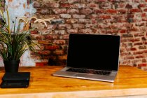 Modern netbook placed on wooden counter in coffee shop with interior in loft style — Stock Photo