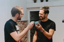 Очарованные мужчины-баристы с маленькими чашками эспрессо дегустации подготовленный кофе во время звон кружки и смотреть друг на друга — стоковое фото