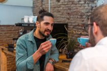 Очарованные мужчины-баристы с маленькими чашками эспрессо дегустации подготовленный кофе во время звон кружки и смотреть друг на друга — стоковое фото