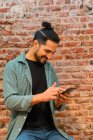 Вид сбоку веселый мужчина-бариста, просматривающий смартфон во время работы в лофт-кафе у обветшалой кирпичной стены — стоковое фото