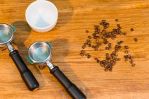 High angle of portafilters placed on wooden table with empty cup and fresh coffee beans in cafe — Stock Photo