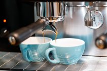 Professionelle Kaffeemaschine, die Kaffee in kleine Keramiktassen im Kaffeehaus mit moderner Ausstattung gießt — Stockfoto