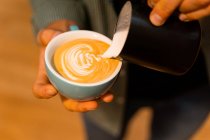 Alto angolo di coltura irriconoscibile barista aggiungendo latte in tazza con caffè mentre prepara gustoso cappuccino — Foto stock