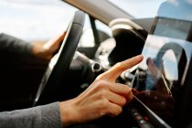 Side view of crop unrecognizable male driver in casual clothes touching screen of GPS navigator while sitting in modern car on sunny day — Stock Photo