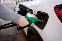 Vista lateral del hombre irreconocible recortado con guantes de plástico llenando el combustible en el coche moderno en la gasolinera durante el día - foto de stock