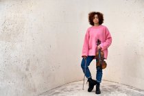 Full body emotionless redhead female musician in casual outfit standing with eyes closed and holding acoustic violin against white concrete wall — Stock Photo