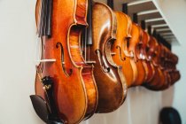 Collection of modern acoustic violins hanging on rack against white wall in contemporary light musical studio — Stock Photo