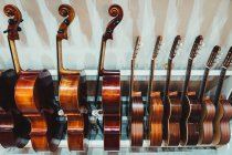 Sammlung moderner akustischer Geigen und Gitarren, die im zeitgenössischen leichten Musikstudio auf einem Regal an einer weißen Wand hängen — Stockfoto
