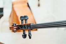 Dünner Geigenhals mit Saiten und Stimmwirbeln gegen weiße Wand in modernem Musikstudio — Stockfoto