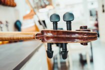 Cuello fino de violín con cuerdas y clavijas de afinación contra pared blanca en estudio musical moderno - foto de stock