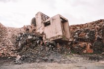 Pedaço de construção de cimento destruído em poço aberto com pedras ásperas sob céu nublado à luz do dia — Fotografia de Stock