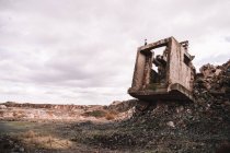 Pedaço de construção de cimento destruído em poço aberto com pedras ásperas sob céu nublado à luz do dia — Fotografia de Stock