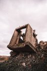 Stück zerstörtes Zementgebäude auf offener Grube mit groben Steinen unter bewölktem Himmel bei Tageslicht — Stockfoto