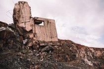 Pièce de ciment détruite à ciel ouvert avec des pierres brutes sous un ciel nuageux à la lumière du jour — Photo de stock