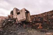 Stück zerstörtes Zementgebäude auf offener Grube mit groben Steinen unter bewölktem Himmel bei Tageslicht — Stockfoto