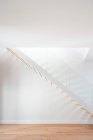 Escalier en bois au-dessus du parquet près du mur blanc avec ombre dans un bâtiment contemporain à la lumière du jour — Photo de stock