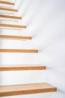 Escadaria de madeira acima do parquet perto da parede branca com sombra no edifício contemporâneo na luz do dia — Fotografia de Stock