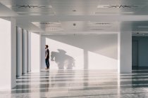 Side view of male standing near window in empty spacious office hallway with shadows and sunlight on white walls and looking away — Stock Photo
