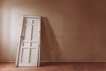 Porta de madeira branca com superfície rasgada colocada na velha sala vazia durante o dia — Fotografia de Stock