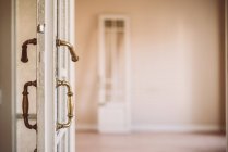 Old fashioned white wooden opened door with ornamental handles in retro style in empty apartment — Stock Photo